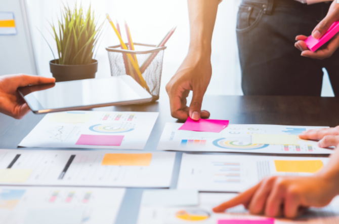 A table with reports on it—people are pointing things out on them and attaching sticky notes.